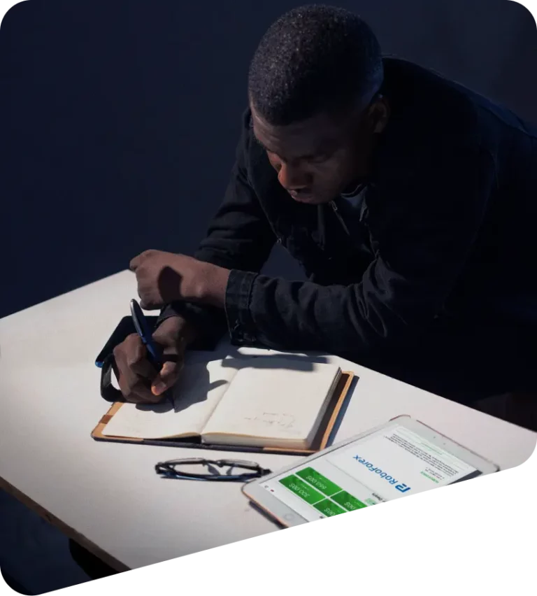 Trader macht Notizen, daneben ein Tablet mit RoboForex